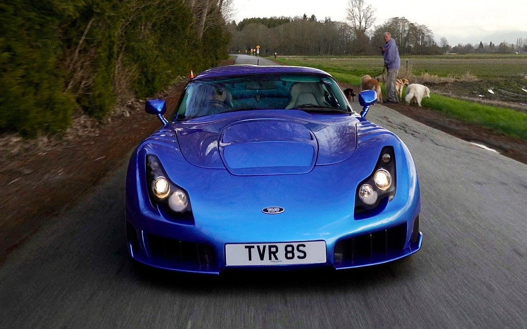 Blue sports car driving on a road with trees and a person in the background